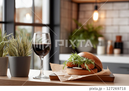 Gourmet Burger with Fresh Greens and Glass of Red Wine on a Wooden Table in Modern Kitchen 127269718
