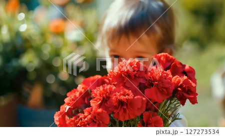 母の日のイメージ。真っ赤なカーネーションの花束の後ろに隠れている幼い子供のクローズアップ 127273534