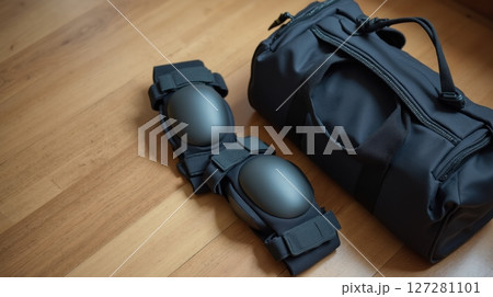 Knee pads next to a sports bag on a wooden floor 127281101