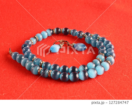 Set of necklace and earrings with blue cat's eye effect. Red background. Zircon inserts 127284747