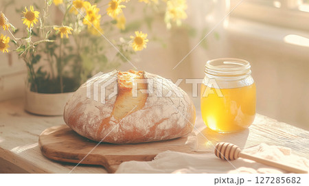 Freshly baked artisan bread and honey on rustic sunlit table with flowers. Charming countryside breakfast, healthy eating and bakery theme 127285682