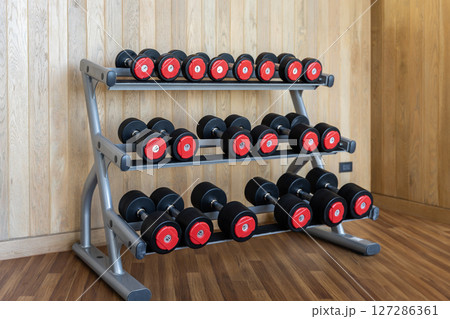 Stand with various dumbbells, weight training equipment, black dumbbell set on rack in modern sport fitness center. Stand with various dumbbells, weight training equipment, black dumbbell set on rack in modern sport fitness center. 127286361