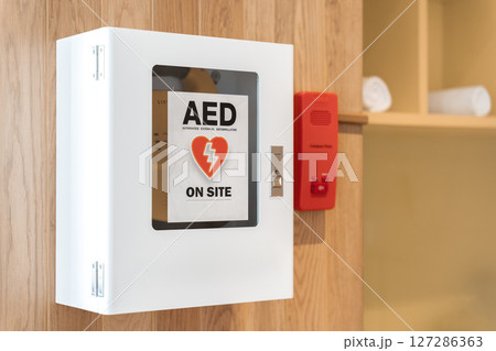 General view of a life saving defibrillator. Portable automated external defibrillator (AED) mounted on the wall in public restroom at airport. 127286363