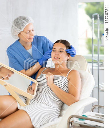 Cosmetologist examine patients contour face after lifting oval of face and palpate cheekbones Cosmetologist examine patients contour face after lifting oval of face and palpate cheekbones 127287244