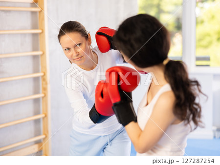 Focused woman practicing boxing punches in sparring during group self defence course Focused woman practicing boxing punches in sparring during group self defence course 127287254