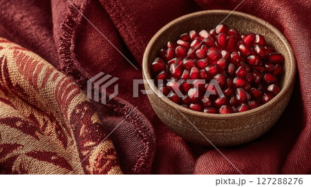 Red Pomegranate Seeds in Rustic Bowl on Maroon Fabric 127288276