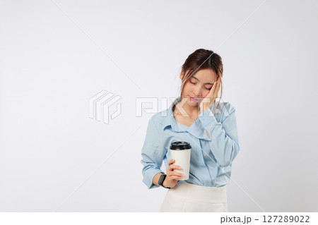 Sleep deprived tired woman covers face with palm, holding coffee paper cup, feeling sad and sleepy, stress from lack of sleep shows in her eyes as she struggles to wake up. isolated white background Sleep deprived tired woman covers face with palm, holding coffee paper cup, feeling sad and sleepy, stress from lack of sleep shows in her eyes as she struggles to wake up. isolated white background 127289022