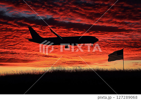 Silhouette of a passenger plane flying low over the earth with the usa flag against a beautiful sunrise or sunset in the sky. Travel concept in the USA. 127289068