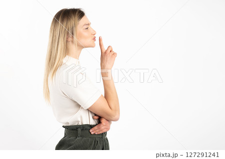 Woman standing profile the camera and showing silence gesture with finger 127291241