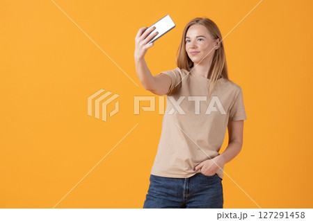 Young Woman Taking a Selfie on a Yellow Background 127291458