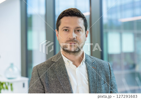 Close-up portrait of a serious young man in a suit standing in the office, looking confidently at the camera. 127291683