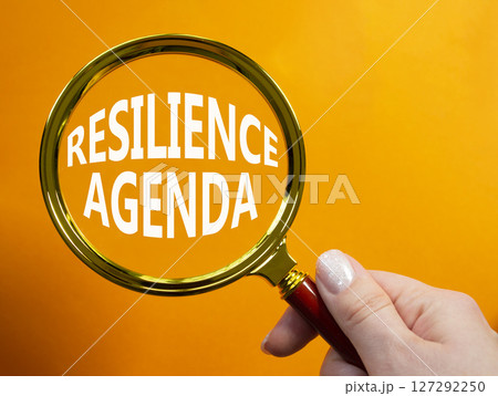 Resilience agenda symbol. Magnifying glass with words Resilience agenda. Beautiful orange background. Businessman hand. Business and Resilience agenda concept. Copy space. Resilience agenda symbol. Magnifying glass with words Resilience agenda. Beautiful orange background. Businessman hand. Business and Resilience agenda concept. Copy space. 127292250