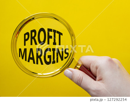 Profit Margins symbol. Magnifying glass with words Profit Margins. Beautiful yellow background. Businessman hand. Business and Profit Margins concept. Copy space. 127292254