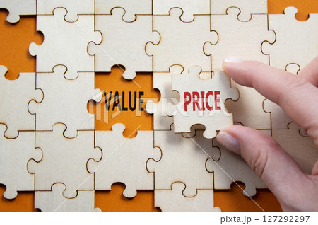 Price and Value symbol. Concept word Price and Value on wooden puzzle. Businessman hand. Beautiful orange background. Business and Price and Value concept. Copy space Price and Value symbol. Concept word Price and Value on wooden puzzle. Businessman hand. Beautiful orange background. Business and Price and Value concept. Copy space 127292297