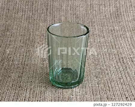 An old faceted vodka glass. In USSR it was called Granchik. An empty glass against a burlap background. An old faceted vodka glass. In USSR it was called Granchik. An empty glass against a burlap background. 127292429