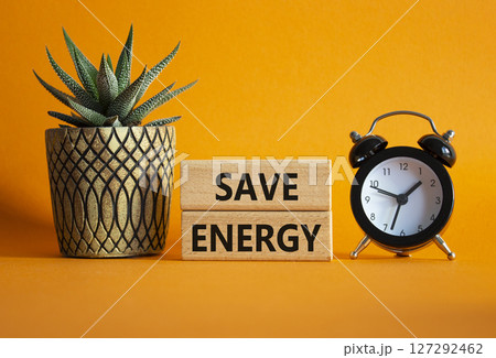 Save Energy symbol. Wooden blocks with words Save Energy. Beautiful orange background with alarm clock and succulent plant. Business and Save Energy concept. Copy space. Save Energy symbol. Wooden blocks with words Save Energy. Beautiful orange background with alarm clock and succulent plant. Business and Save Energy concept. Copy space. 127292462