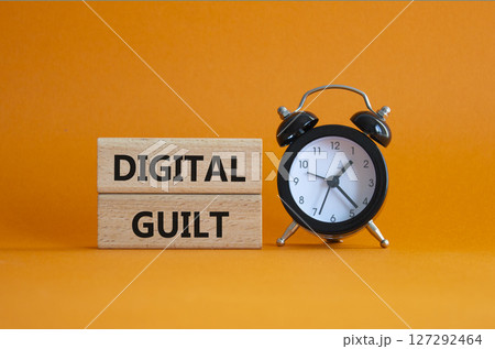 Digital Guilt symbol. Concept words Digital Guilt on wooden blocks. Beautiful orange background with alarm clock. Business and Digital Guilt concept. Copy space. 127292464