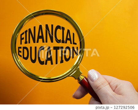 Financial Education symbol. Magnifying Glass with Concept word Financial Education. Businessman hand. Beautiful orange background. Business and Financial Education concept. Copy space 127292506
