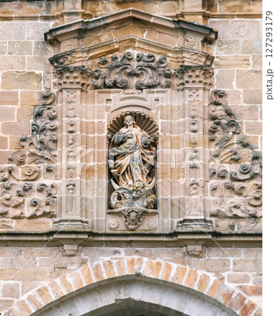 Carved stone sculpture of a figure surrounded by decorative elements on a historical building Carved stone sculpture of a figure surrounded by decorative elements on a historical building 127293179