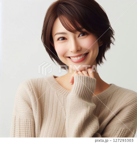 High-resolution photo of a smiling Japanese woman with her hand on her chin, wearing a beige sweater, natural lighting against a clean white backdrop. 127293303
