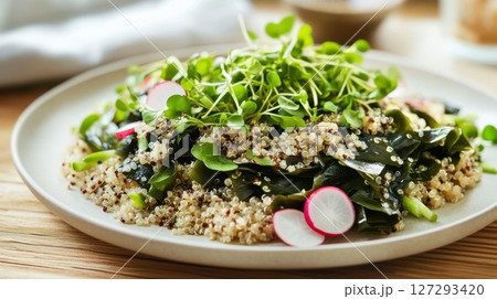 Warm salad with tender wakame seaweed and quinoa, drizzled with silky truffle sauce on a minimalist white plate, garnished with thin radish slices and microgreens, high-quality food styling 127293420