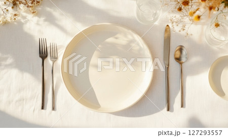 Table set with mix of old porcelain plates and modern flatware, dried flowers, linen tablecloth, morning sunlight 127293557