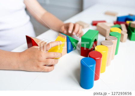 Child engaging with colorful geometric wooden blocks on white table 127293656