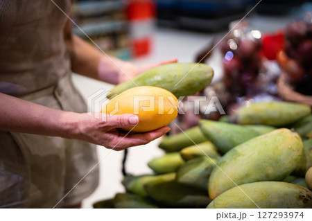Woman hand selecting ripe mango fruit from variety on market counter for healthy diet choice 127293974