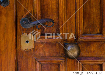 Old wooden door of Athens Greece features antique door handle, brass door knob, and keyhole, reflecting the historical architecture and traditional craftsmanship found in the city. Old wooden door of Athens Greece features antique door handle, brass door knob, and keyhole, reflecting the historical architecture and traditional craftsmanship found in the city. 127294163