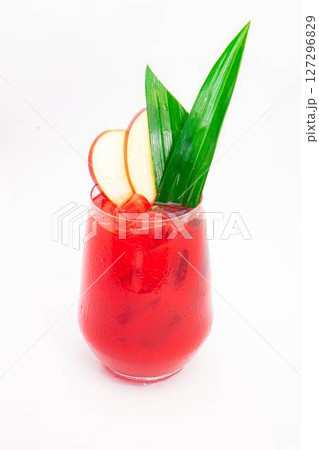 red apple cocktail with ice served in clear glass and garnished with tropical green leaves and apple slices on white background. High quality photo 127296829