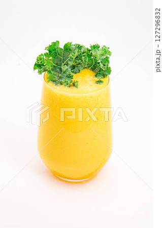 yellow fruit smoothie or juice served in clear glass and garnished with fresh curly kale on clean white background. High quality photo 127296832
