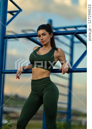 Girl in athletic wear confidently poses on sports ground with vibrant sky and sea in background Capturing essence of fitness and beauty at dusk Girl in athletic wear confidently poses on sports ground with vibrant sky and sea in background Capturing essence of fitness and beauty at dusk 127299028
