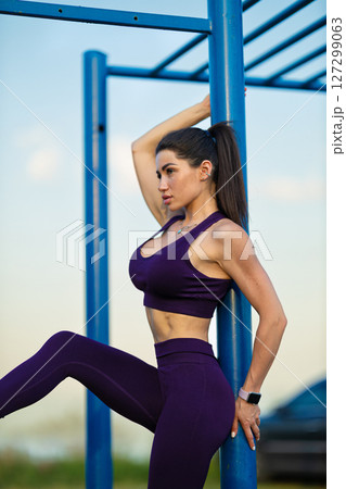 sporty girl confidently poses near a blue structure on a sports ground alongside the sea The environment is bright, highlighting her active lifestyle and dedication to fitness 127299063