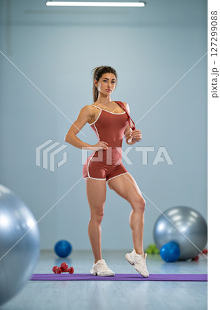 girl stands confidently in a gym, showcasing her sporty attire She strikes a pose while surrounded by gym equipment, including exercise balls and weights, emphasizing her athleticism girl stands confidently in a gym, showcasing her sporty attire She strikes a pose while surrounded by gym equipment, including exercise balls and weights, emphasizing her athleticism 127299088