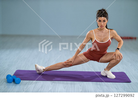 sporty girl is engaged in a left lunge stretch on a purple fitness mat, enhancing her flexibility and strength indoors She focuses on her form in a well lit gym environment sporty girl is engaged in a left lunge stretch on a purple fitness mat, enhancing her flexibility and strength indoors She focuses on her form in a well lit gym environment 127299092