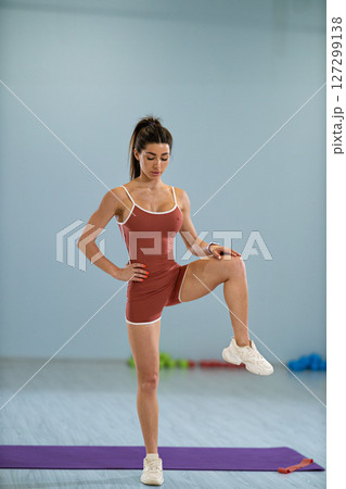 girl athlete is engaged in a standing side knee raise demonstrating her fitness skills in a well lit exercise studio. The setup includes workout equipment and a purple mat. 127299138