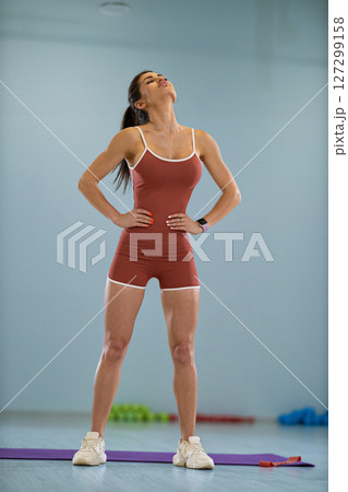 In a spacious training facility a girl athlete tilts her head to the right and left as part of her workout routine. She focuses on balancing and improving her coordination. 127299158