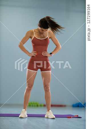 girl athlete performs head rotations in a circular motion to improve her coordination and balance. She is focusing intently in a training studio filled with exercise equipment. 127299164