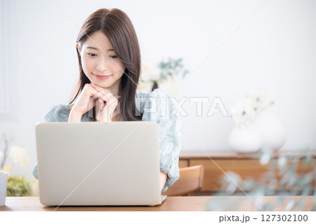 自宅の部屋でパソコンを使う若いかわいいカジュアルな服の女性 127302100
