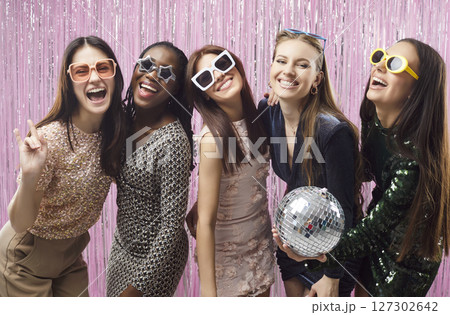 Happy women friends group holding disco ball standing on studio pink foil background. Happy women friends group holding disco ball standing on studio pink foil background. 127302642