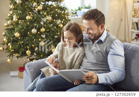 Child looking through family photo album with father enjoying Christmas or New Year eve at home. Child looking through family photo album with father enjoying Christmas or New Year eve at home. 127302659