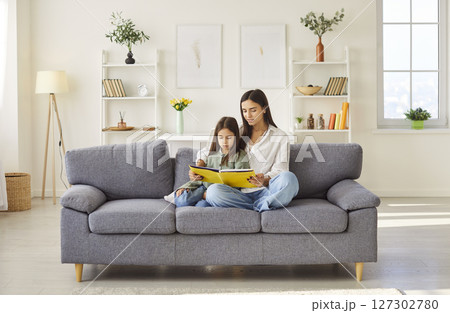 Mother and daughter reading book, story on sofa, happy time at home, joy with preschool child  127302780