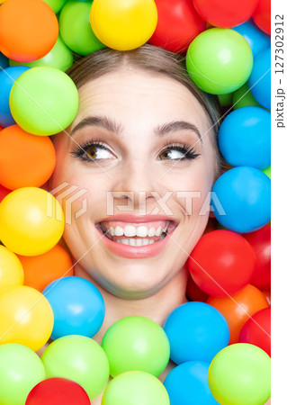 Beautiful woman close-up studio portrait in colorful balls background Beautiful woman close-up studio portrait in colorful balls background 127302912