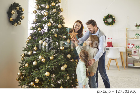 Happy family gathering for Christmas, decorating their home together, placing star on Christmas tree 127302916