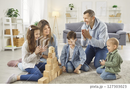 Happy parents playing educational game with children, building wooden block tower together at home. Happy parents playing educational game with children, building wooden block tower together at home. 127303023