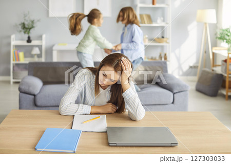 Young tired woman in noisy room, nanny, baby sitter mother suffers from headache touching head  127303033