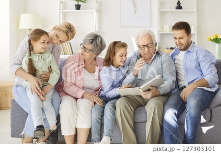 Family Looking At Photo Album And Sharing Memories On Couch At Home 127303101