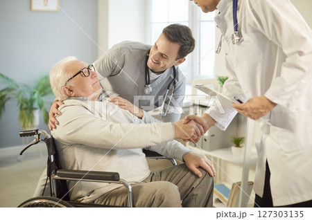 Doctor And Nurse Shaking Hands With Patient In Wheelchair During Consultation Doctor And Nurse Shaking Hands With Patient In Wheelchair During Consultation 127303135