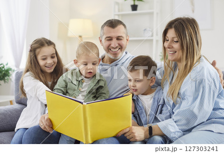Young happy family of five reading a book with children sitting on the sofa at home together. Young happy family of five reading a book with children sitting on the sofa at home together. 127303241