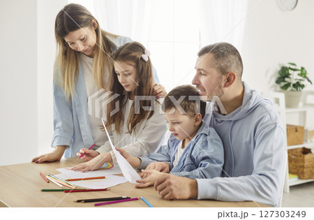 Caring parents and two children sitting at desk, drawing and coloring together during family time. 127303249